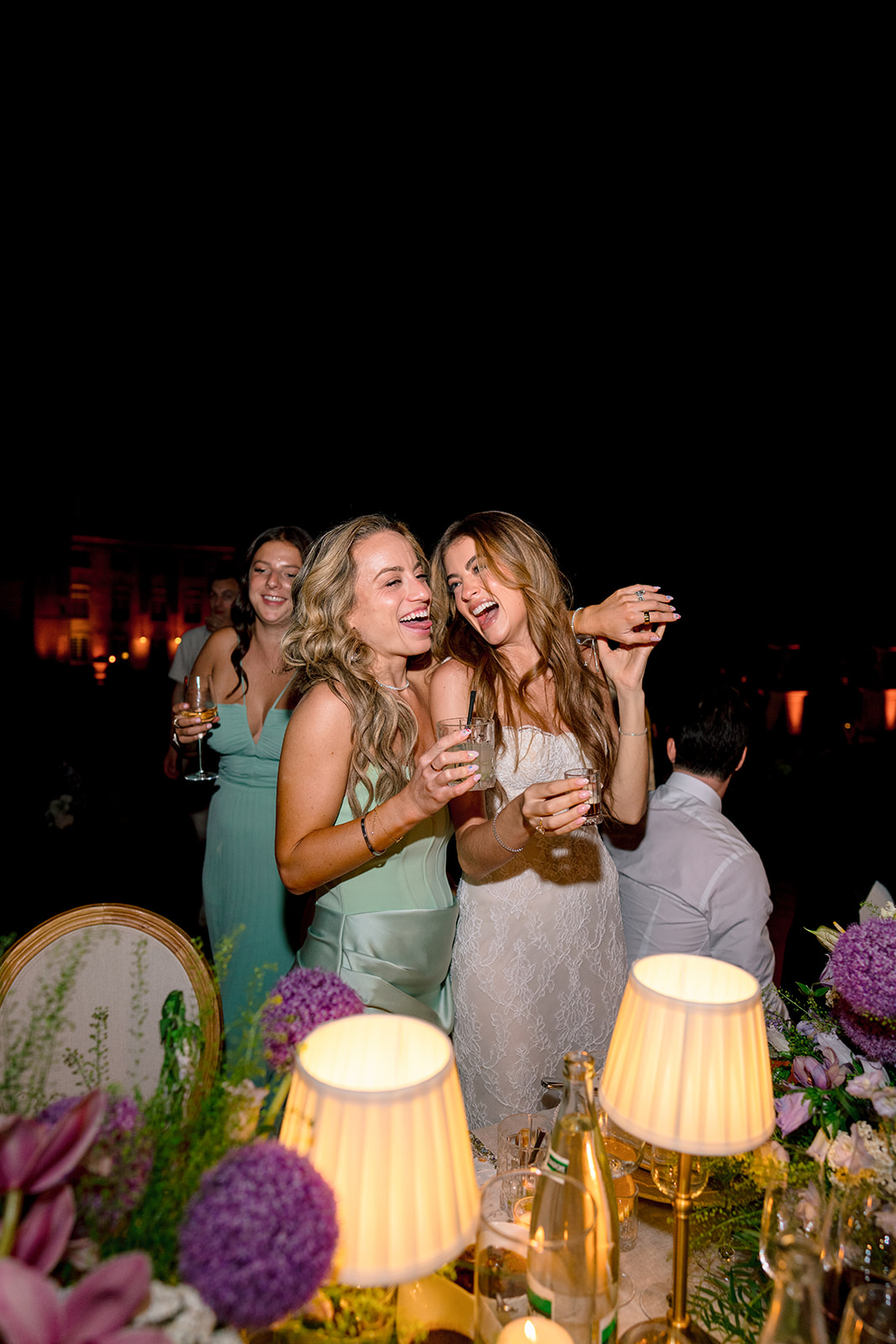 Bride laughing with a friend beside the floral reception tables at Villa Baulieu